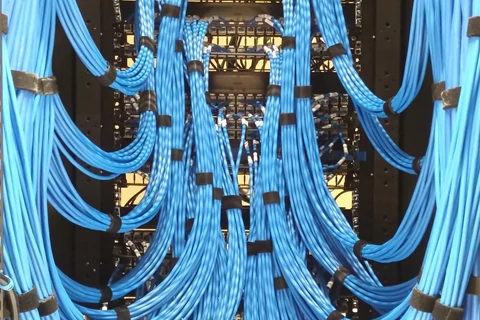 Bir ağ dolabındaki patch panel; sıra sıra numaralı portlara renkli kablolar takılı, kablolar aşağıya doğru toplanıyor.