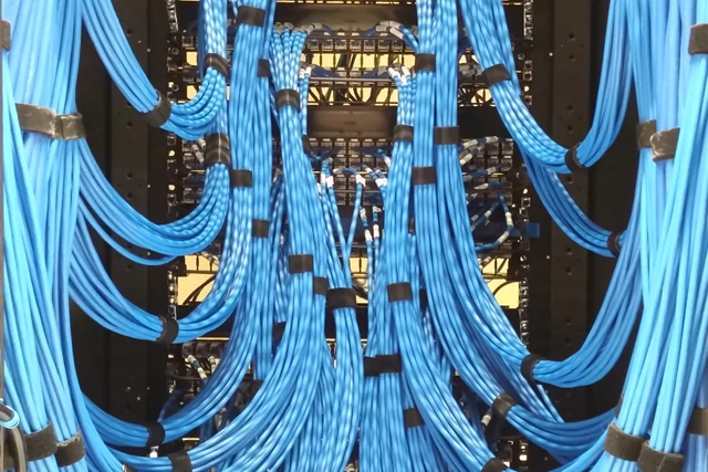 Bir ağ dolabındaki patch panel; sıra sıra numaralı portlara renkli kablolar takılı, kablolar aşağıya doğru toplanıyor.