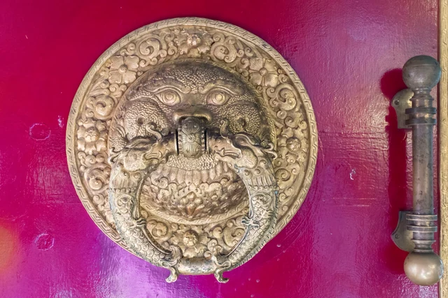 Koyu pembe bir kapıya monte edilmiş, aslan başı biçiminde işlemeli pirinç kapı tokmağı.